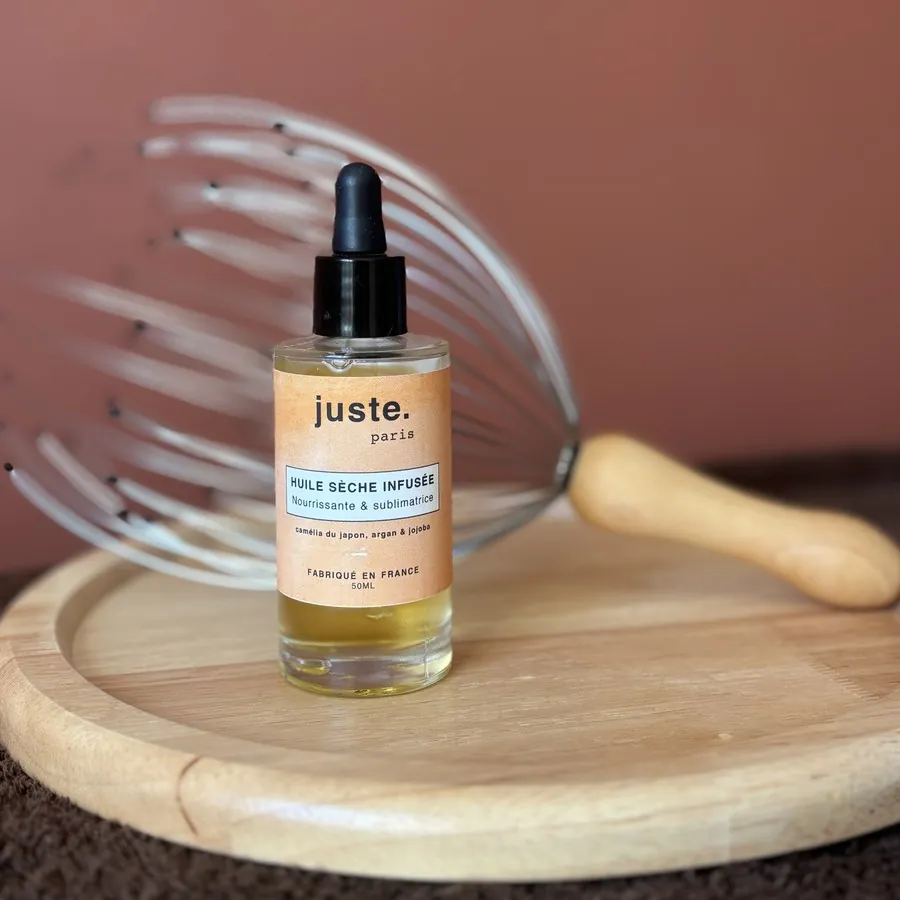 Flacon d'huile sèche infusée et son compte-gouttes, devant un masseur de cuir chevelu